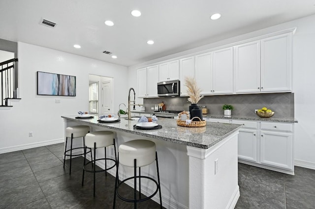 kitchen featuring stainless steel microwave, stove, white cabinetry, and an island with sink