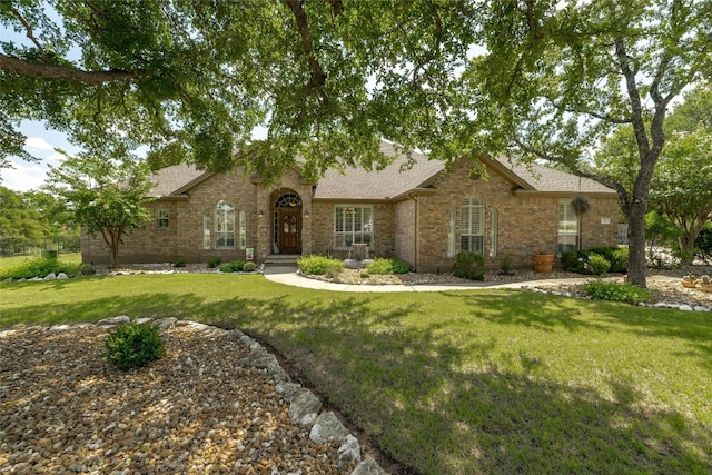 view of front of home with brick siding, a shingled roof, and a front yard