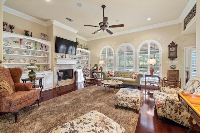 living room with dark wood finished floors, a glass covered fireplace, visible vents, and crown molding