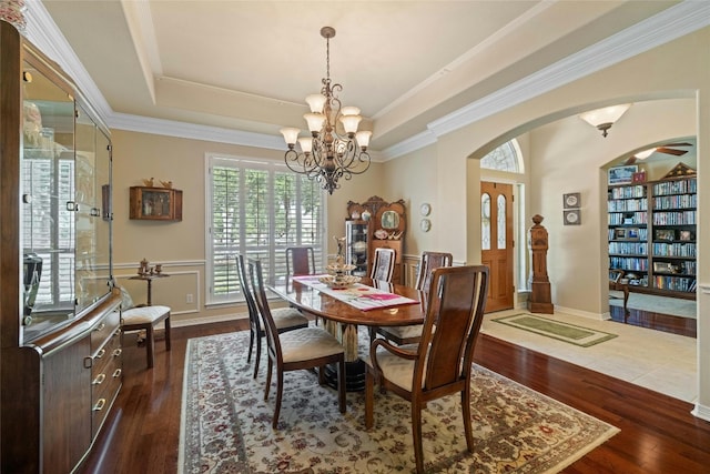 dining area with a tray ceiling, a notable chandelier, dark wood finished floors, and arched walkways