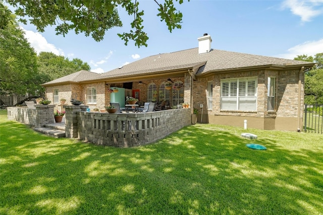 back of house featuring a chimney, brick siding, a lawn, and a patio area