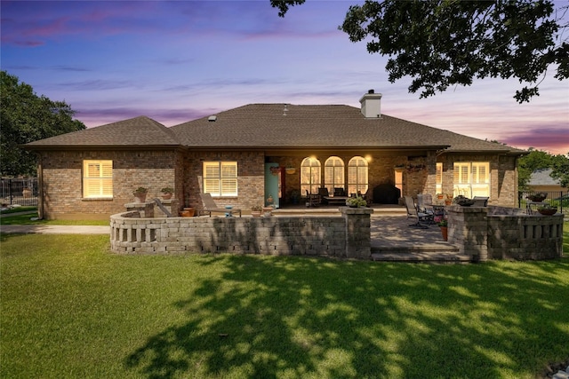 back of property with a chimney, roof with shingles, a yard, a patio area, and brick siding