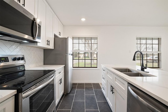 kitchen with stainless steel appliances, white cabinets, a sink, and backsplash