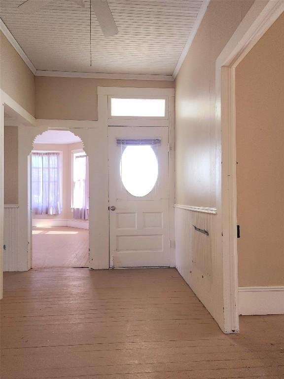 entrance foyer featuring arched walkways, light wood-style floors, a ceiling fan, and crown molding