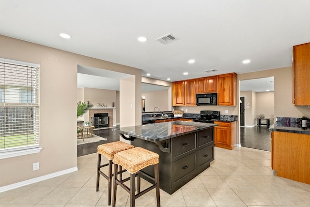 kitchen featuring a sink, visible vents, open floor plan, black appliances, and a kitchen bar