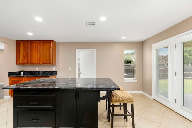 kitchen featuring dark stone countertops, a center island, dark cabinetry, and a kitchen breakfast bar