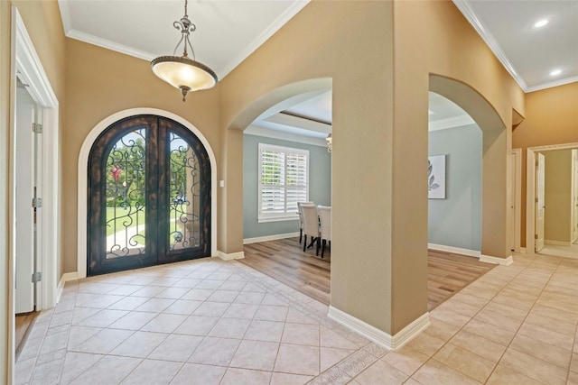 entryway with arched walkways, light tile patterned floors, baseboards, french doors, and ornamental molding