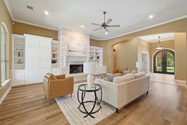 living room featuring arched walkways, french doors, a stone fireplace, and light wood finished floors