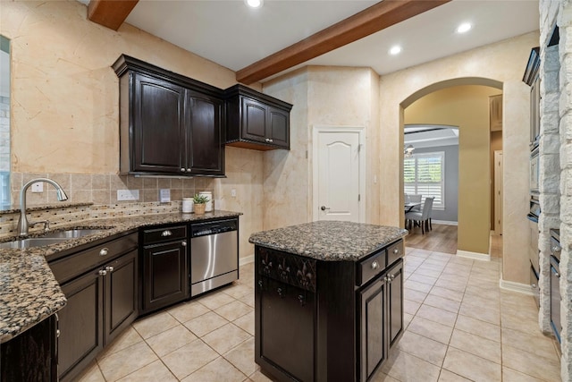 kitchen featuring arched walkways, a kitchen island, a sink, stainless steel dishwasher, and beam ceiling