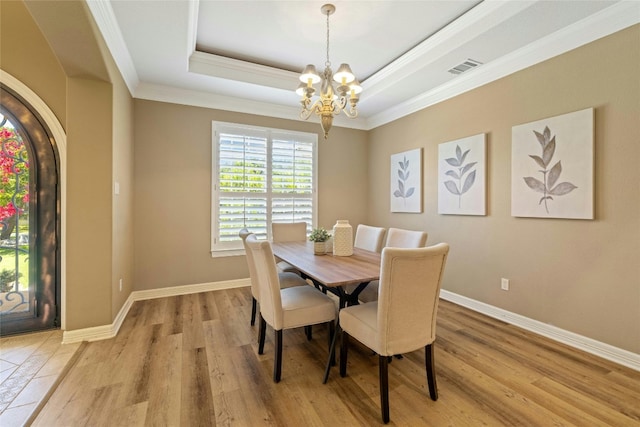 dining area with visible vents, a tray ceiling, light wood-style flooring, and an inviting chandelier