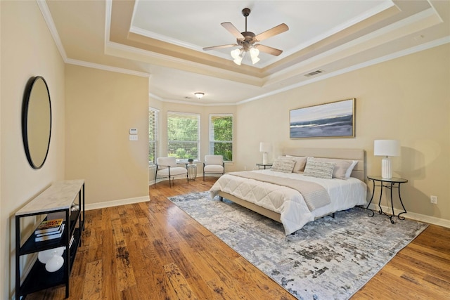 bedroom with a tray ceiling, wood finished floors, and visible vents