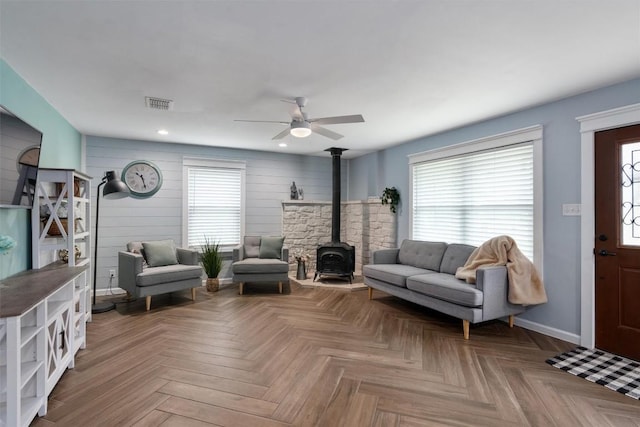 living area featuring a wood stove, visible vents, ceiling fan, and a healthy amount of sunlight