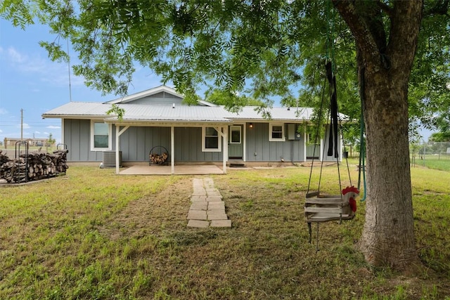 back of house with central air condition unit, metal roof, board and batten siding, and a yard