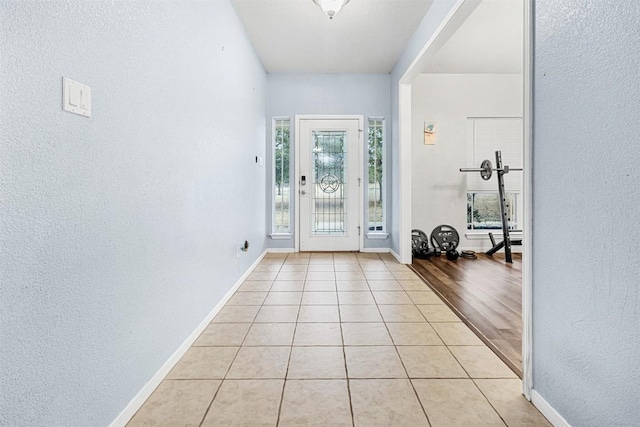 doorway to outside featuring light tile patterned floors, baseboards, and a textured wall