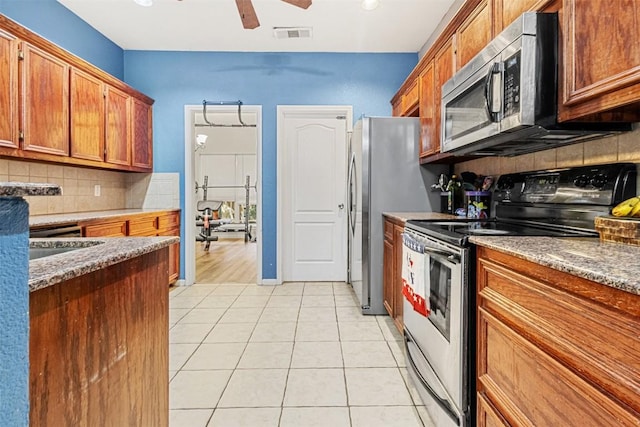 kitchen featuring light tile patterned floors, decorative backsplash, brown cabinetry, ceiling fan, and appliances with stainless steel finishes