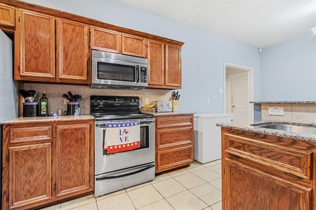 kitchen featuring light tile patterned floors, stainless steel appliances, brown cabinetry, and backsplash