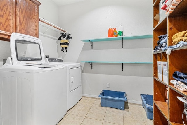 laundry area featuring light tile patterned floors, washing machine and dryer, cabinet space, and baseboards