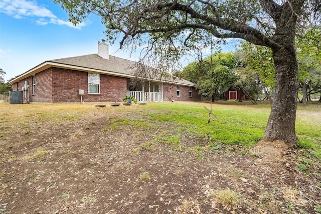 rear view of property featuring brick siding, a lawn, and a chimney