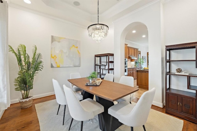 41 Tiburon Dr, The Hills, TX 78738 - dining space with arched walkways, light wood-type flooring, a chandelier, a raised ceiling, and ornamental molding
