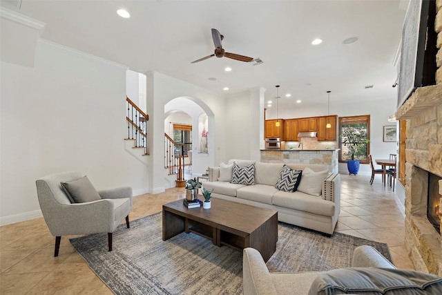 living room featuring ornamental molding, a stone fireplace, baseboards, and light tile patterned floors