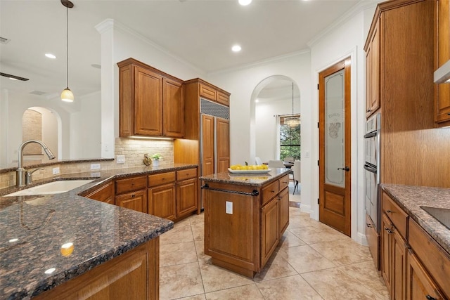 41 Tiburon Dr, The Hills, TX 78738 - kitchen with arched walkways, brown cabinetry, decorative backsplash, dark stone countertops, and ornamental molding