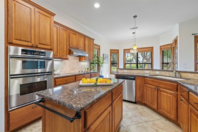 kitchen with under cabinet range hood, a sink, appliances with stainless steel finishes, a center island, and brown cabinetry