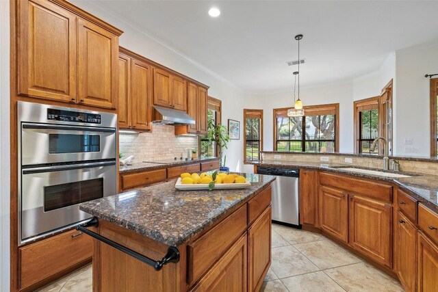 41 Tiburon Dr, The Hills, TX 78738 - kitchen with stainless steel appliances, brown cabinetry, decorative backsplash, crown molding, and recessed lighting