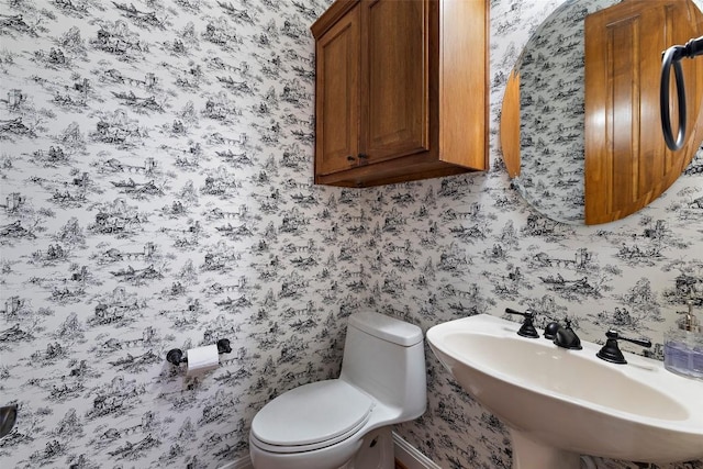 bathroom with a sink, toilet, and wallpapered walls