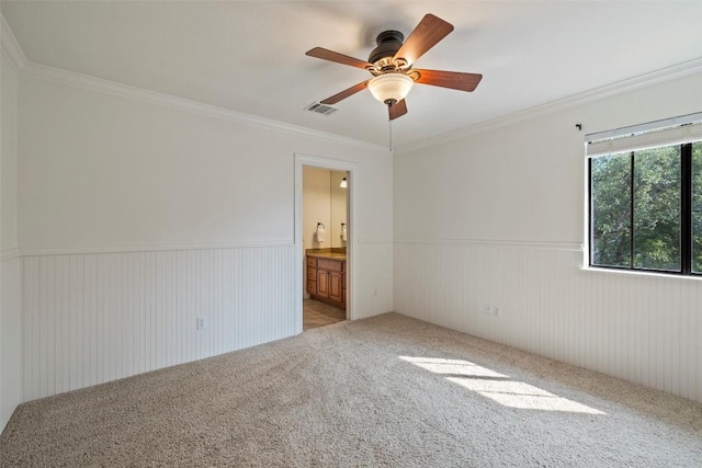 unfurnished bedroom featuring light colored carpet, a wainscoted wall, visible vents, and crown molding