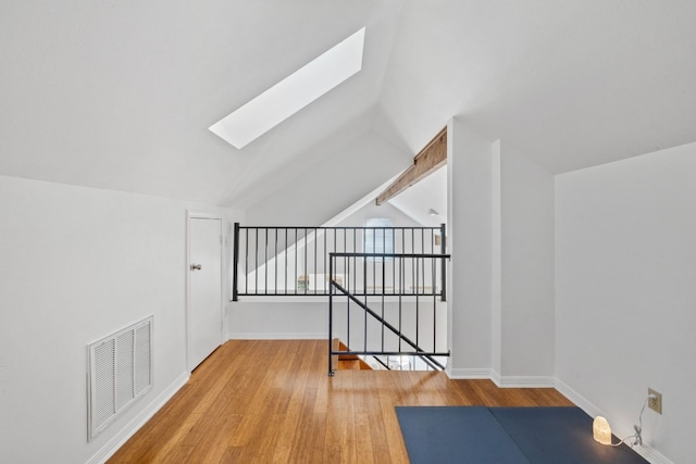 additional living space featuring baseboards, vaulted ceiling with skylight, visible vents, and wood finished floors