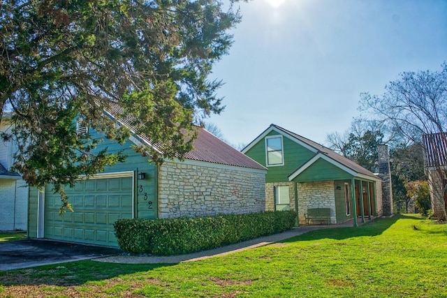 view of front facade featuring driveway, a garage, stone siding, metal roof, and a front lawn