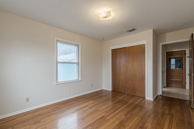 unfurnished bedroom featuring baseboards, a closet, visible vents, and wood finished floors