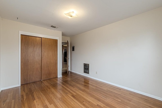 unfurnished bedroom featuring heating unit, a closet, visible vents, light wood-style flooring, and baseboards