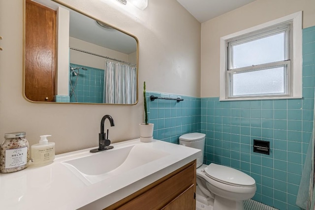 bathroom with toilet, a wainscoted wall, a shower with shower curtain, vanity, and tile walls