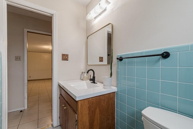 half bath featuring tile walls, toilet, wainscoting, vanity, and tile patterned floors