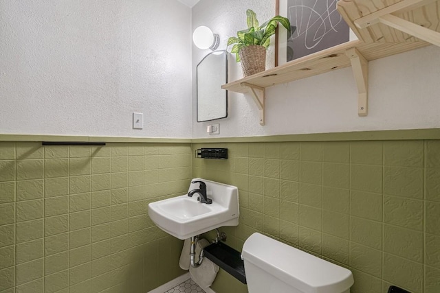 half bathroom with a wainscoted wall, a sink, toilet, and tile walls