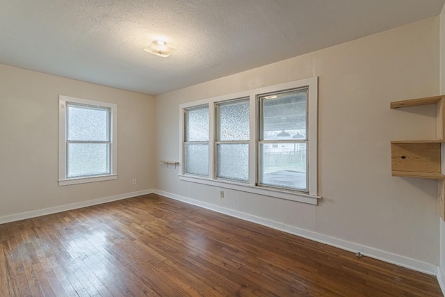 spare room with a textured ceiling, dark wood finished floors, and baseboards