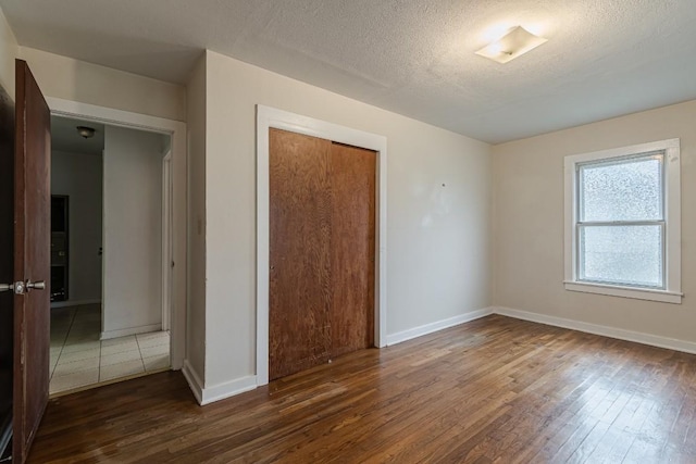 unfurnished room featuring dark wood finished floors, a textured ceiling, and baseboards