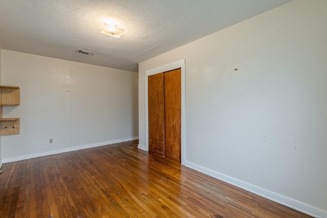 empty room with dark wood-style floors, a textured ceiling, visible vents, and baseboards