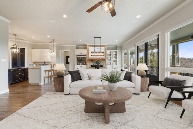 living area with crown molding, recessed lighting, a large fireplace, ceiling fan, and wood finished floors