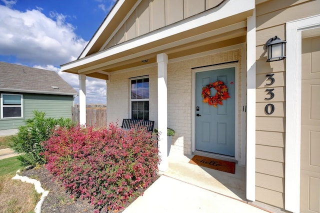 doorway to property with board and batten siding, covered porch, and brick siding