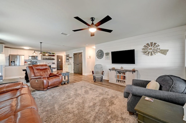 living room featuring light wood-style floors, ceiling fan, visible vents, and baseboards