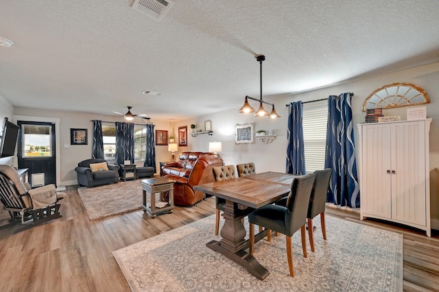 dining room with a textured ceiling, light wood-type flooring, visible vents, and a ceiling fan