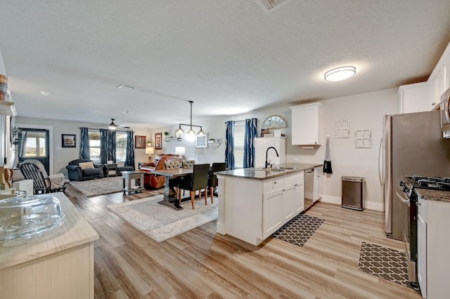 kitchen featuring stainless steel appliances, hanging light fixtures, open floor plan, white cabinetry, and a sink