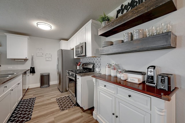 kitchen featuring a textured ceiling, stainless steel appliances, light wood-style floors, white cabinets, and backsplash