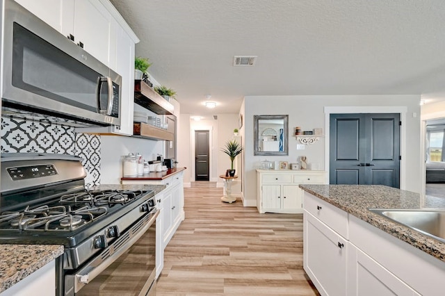 kitchen with light wood finished floors, visible vents, appliances with stainless steel finishes, white cabinetry, and light stone countertops