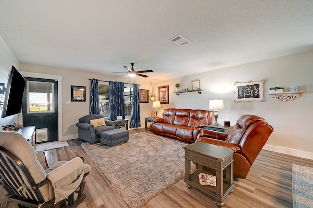 living room featuring light wood finished floors, visible vents, ceiling fan, a textured ceiling, and baseboards