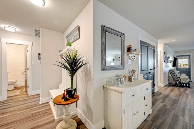 hallway with baseboards, a textured ceiling, visible vents, and wood finished floors