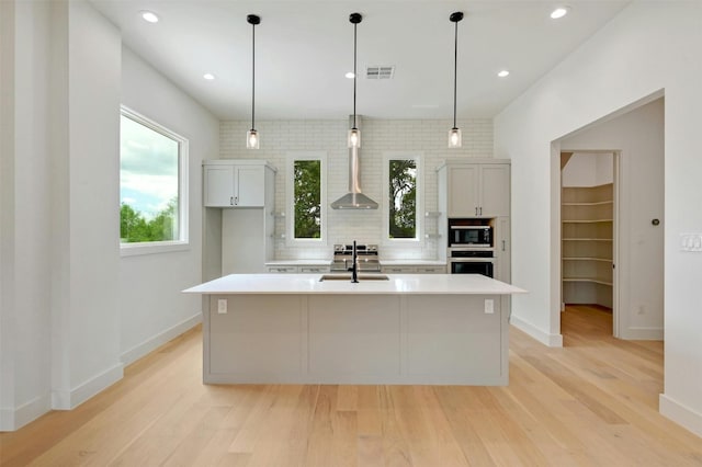 kitchen with a sink, light countertops, appliances with stainless steel finishes, hanging light fixtures, and an island with sink