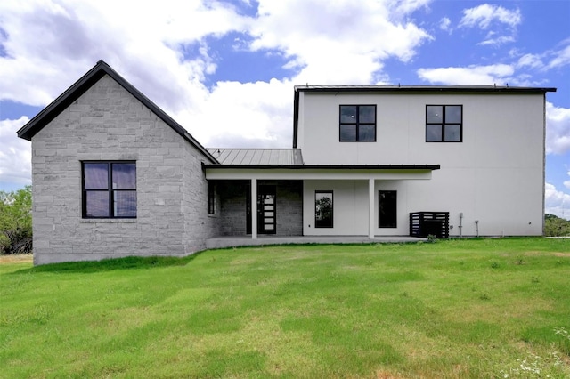 back of property with metal roof, a standing seam roof, stone siding, and a lawn